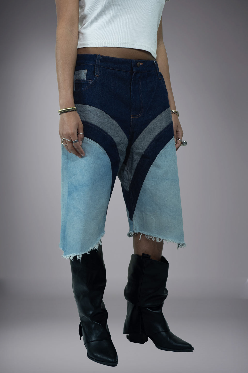 ide view of two-tone denim long shorts with dark raw denim panels, light wash inserts, curved contrast seams and raw frayed hem.