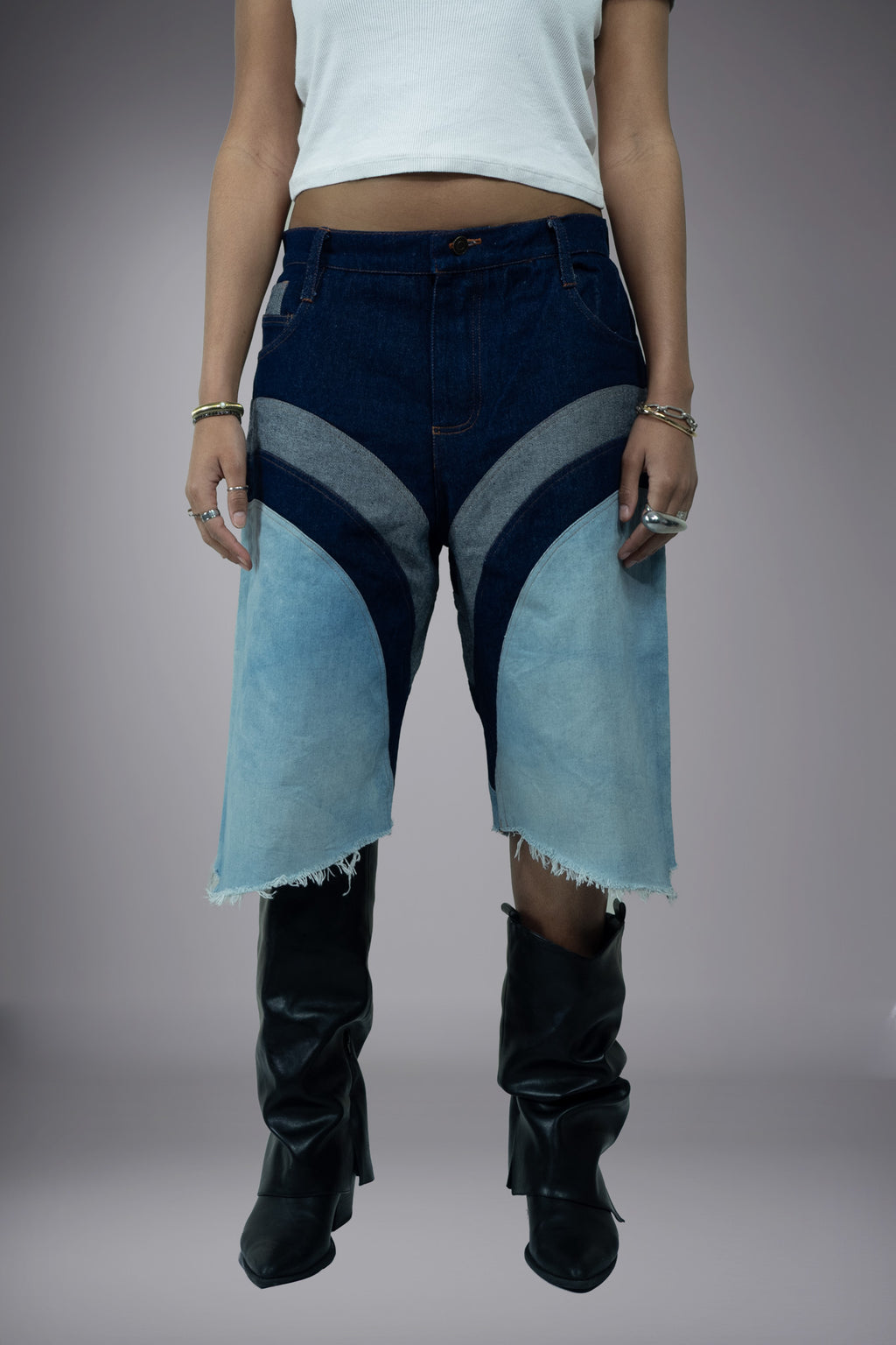 Front view of two-tone denim long shorts with dark raw denim waistband, light wash panels, curved seam construction and raw frayed hems.
