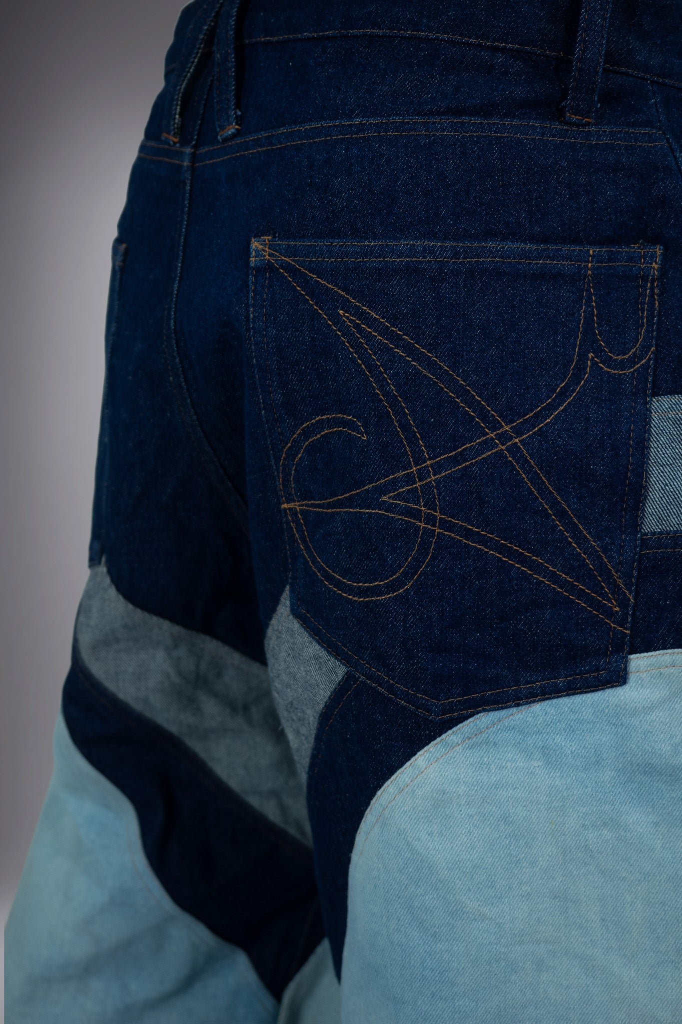 close-up back detail of two-tone denim long shorts with graphic pocket stitching, dark raw denim panels and light wash inserts.