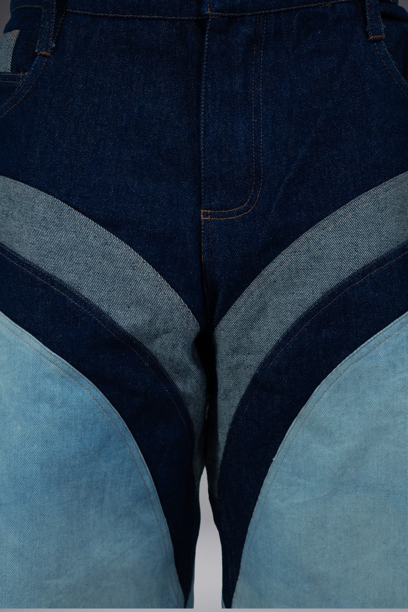 Close-up front detail of two-tone denim long shorts with curved light wash panels, dark raw denim construction and contrast stitching.