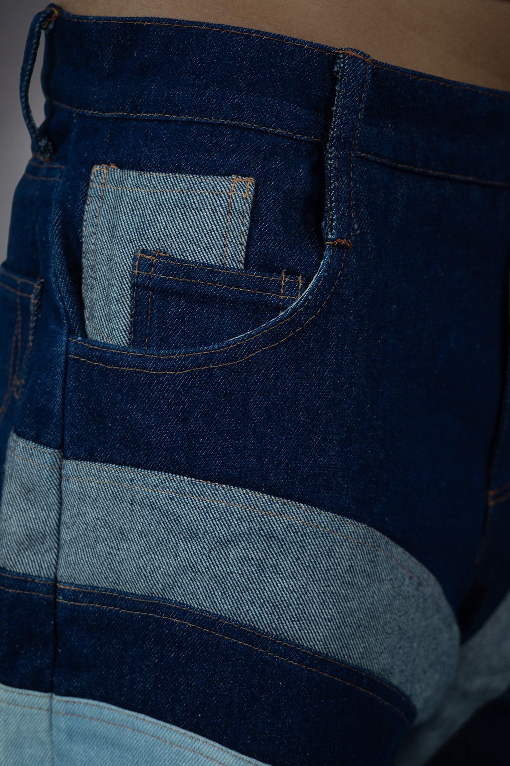 Close-up side pocket detail of two-tone denim long shorts with dark raw denim, light wash pocket insert and curved panel construction.