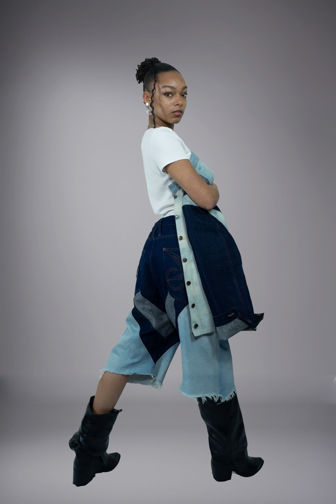 Side view of two-tone denim long shorts with curved dark denim panels, light wash inserts, raw frayed hems and button side detailing.