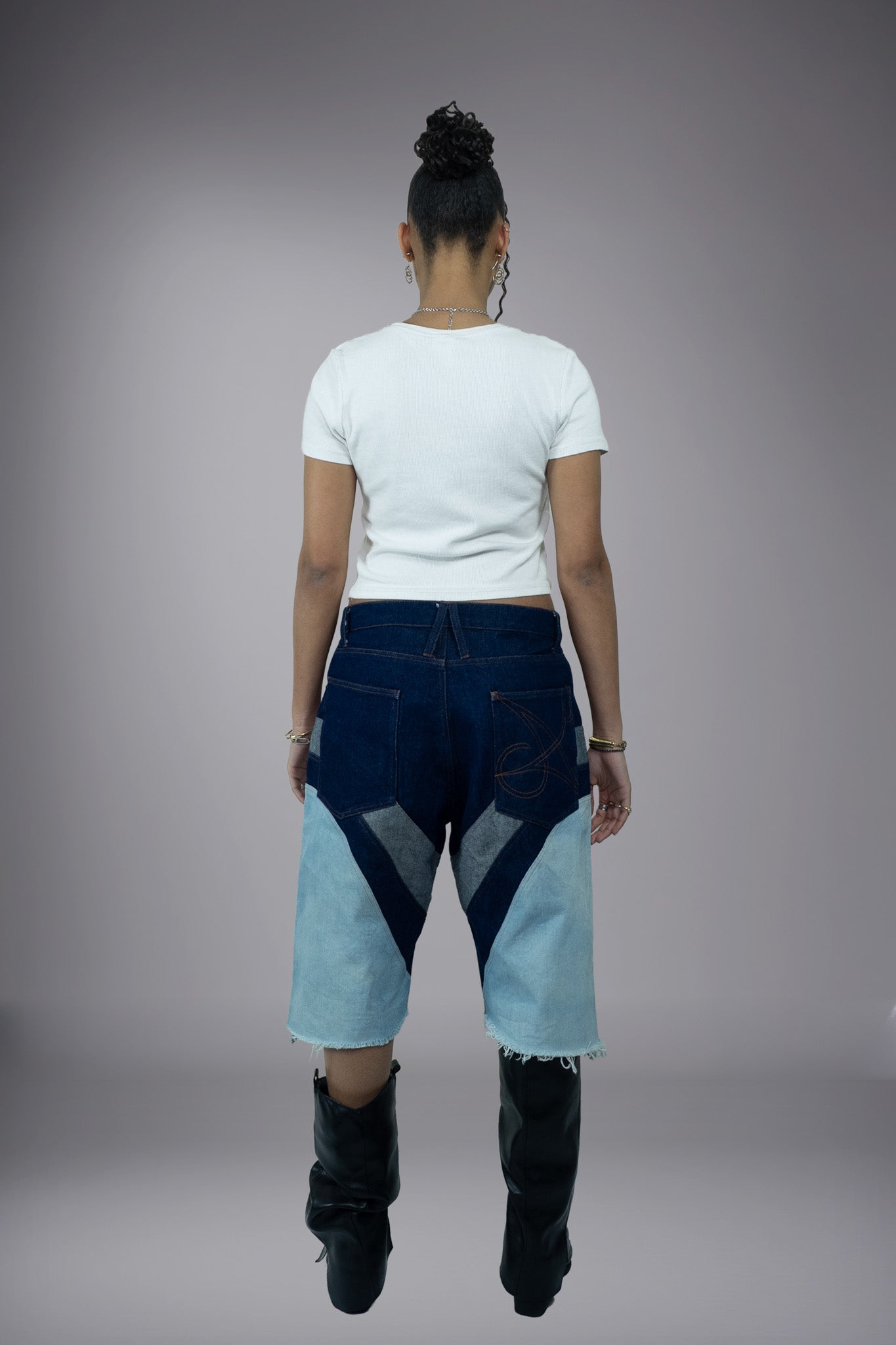 Full back view of two-tone denim long shorts with dark raw denim pockets, graphic pocket stitching, light wash panels and raw frayed hems.