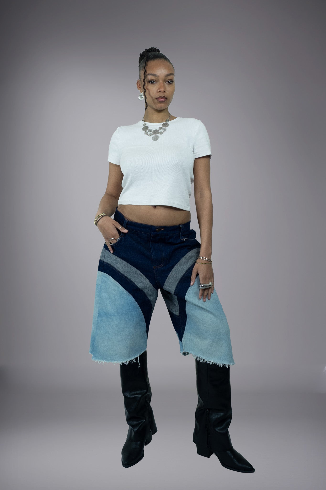 Full front view of two-tone denim long shorts with dark raw denim top block, light wash panels, curved seam construction and raw frayed hems.