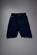 Flat lay of dark raw denim long shorts with curved contrast stitching, wide-leg cut and raw frayed hems.