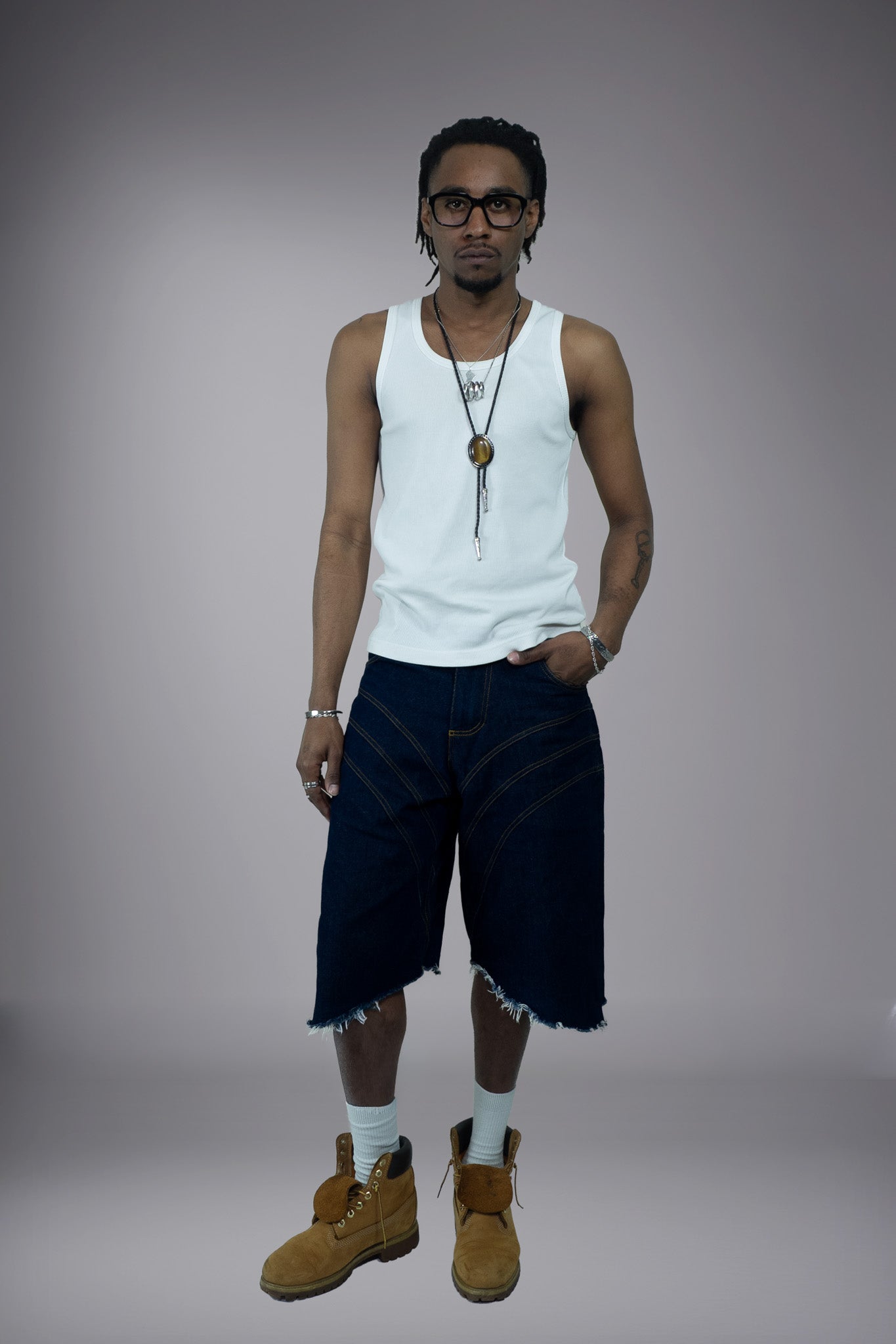 Full front view of dark raw denim long shorts with curved seam construction, contrast stitching and raw frayed hem.