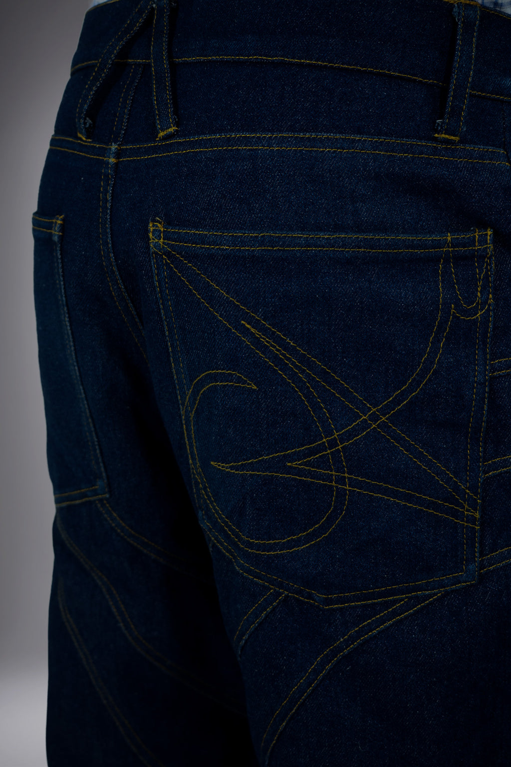 Close-up back detail of dark raw denim long shorts with graphic pocket stitching, contrast seams and structured waistband.