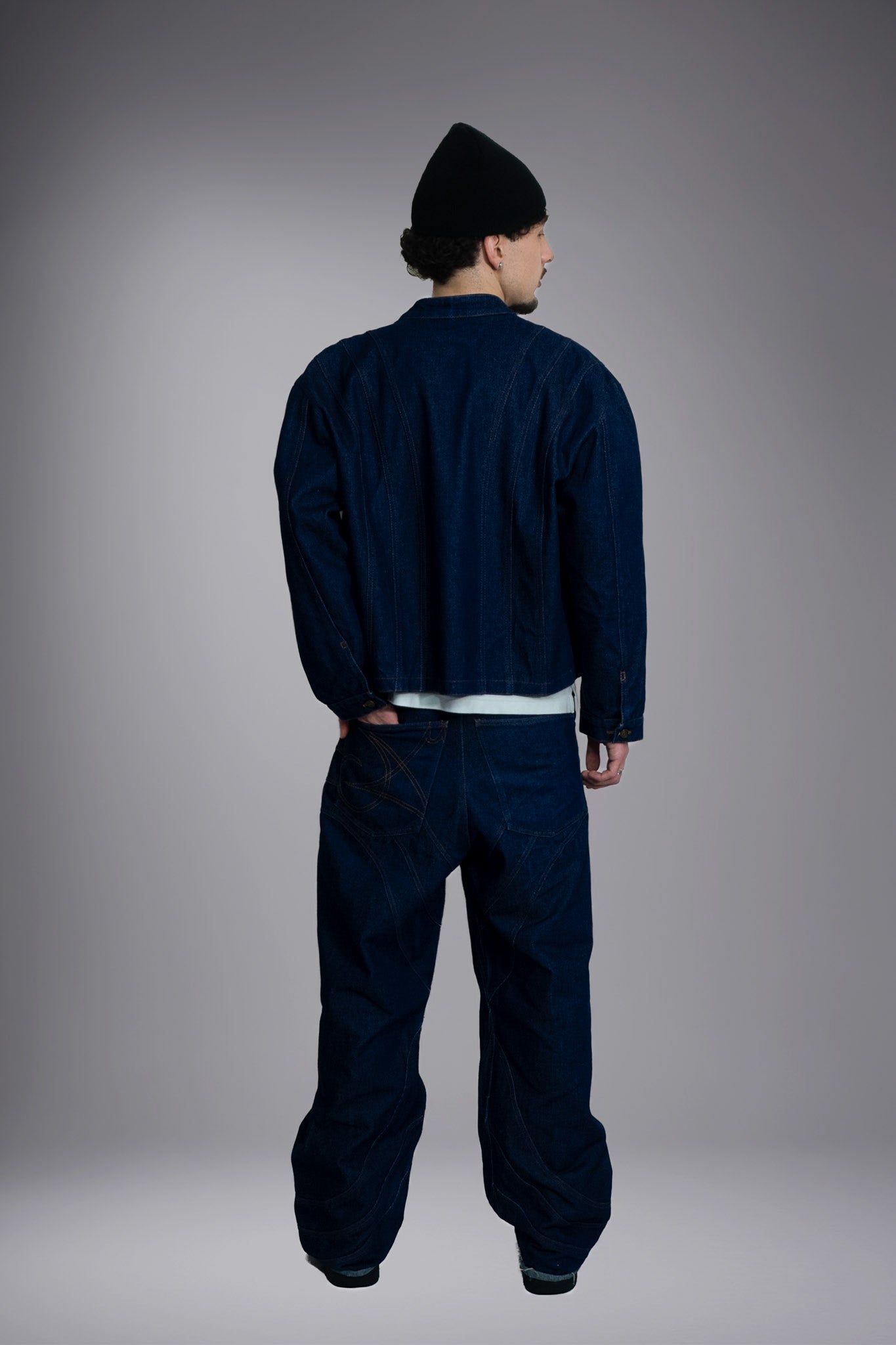 Full-body back view of a dark raw denim jacket and matching baggy jeans with graphic seam details. - Motor Cycle Brut