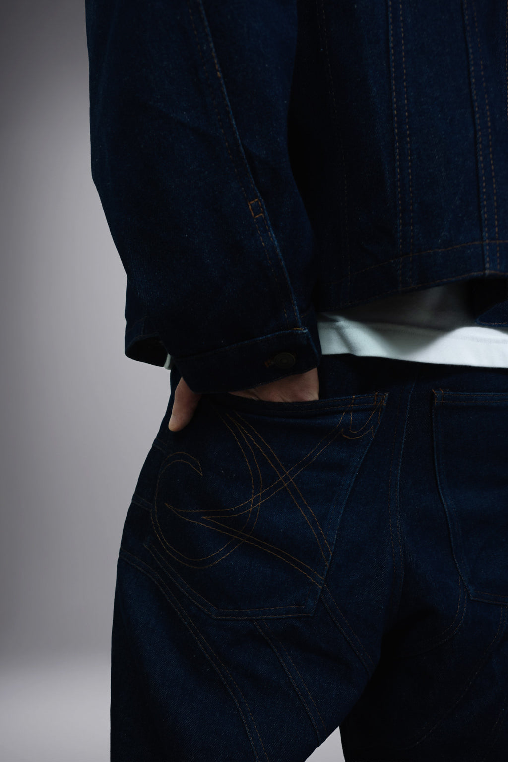 Close-up back detail of dark raw denim jeans with graphic pocket stitching and curved seam panels. - Motor Cycle Brut