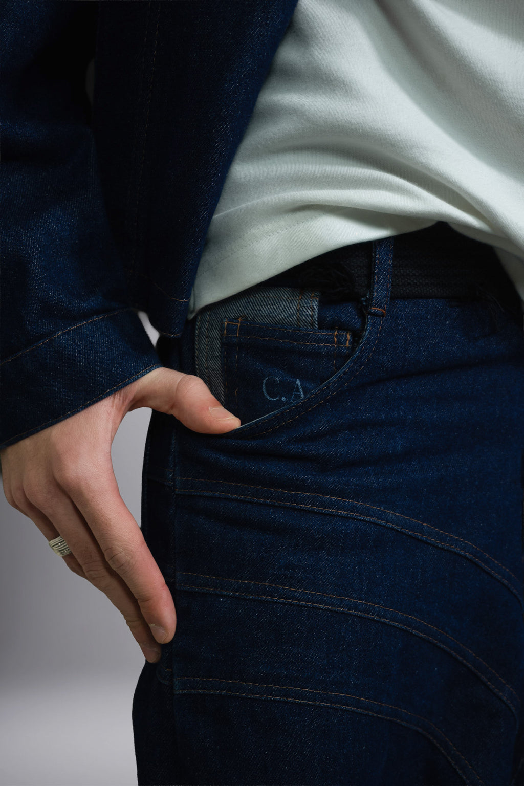 Close-up of dark raw denim jeans with contrast stitching, curved seam details and a visible pocket label. - Motor Cycle Brut