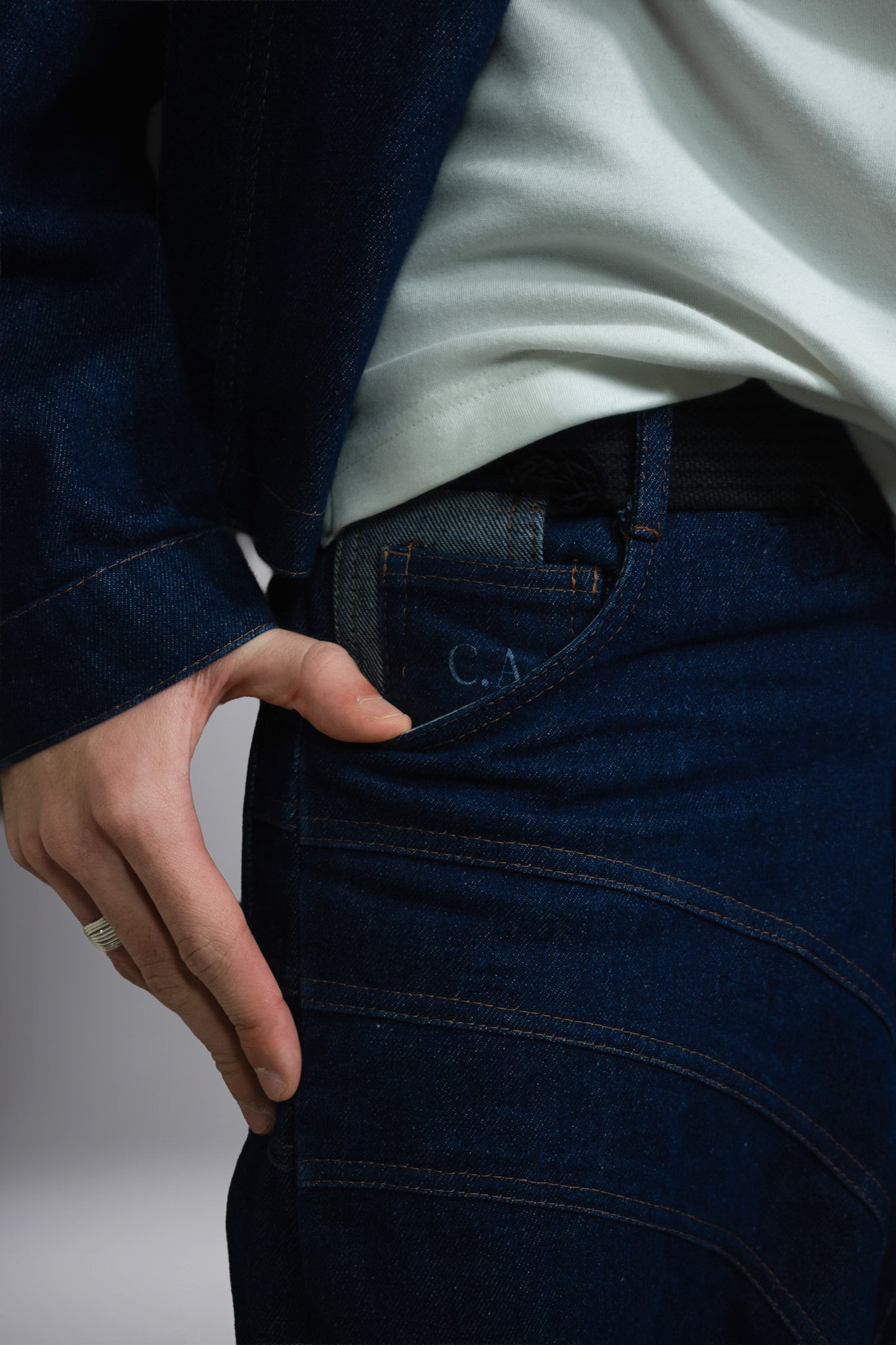 Close-up of dark raw denim jeans with contrast stitching, curved seam details and a visible pocket label. - Motor Cycle Brut