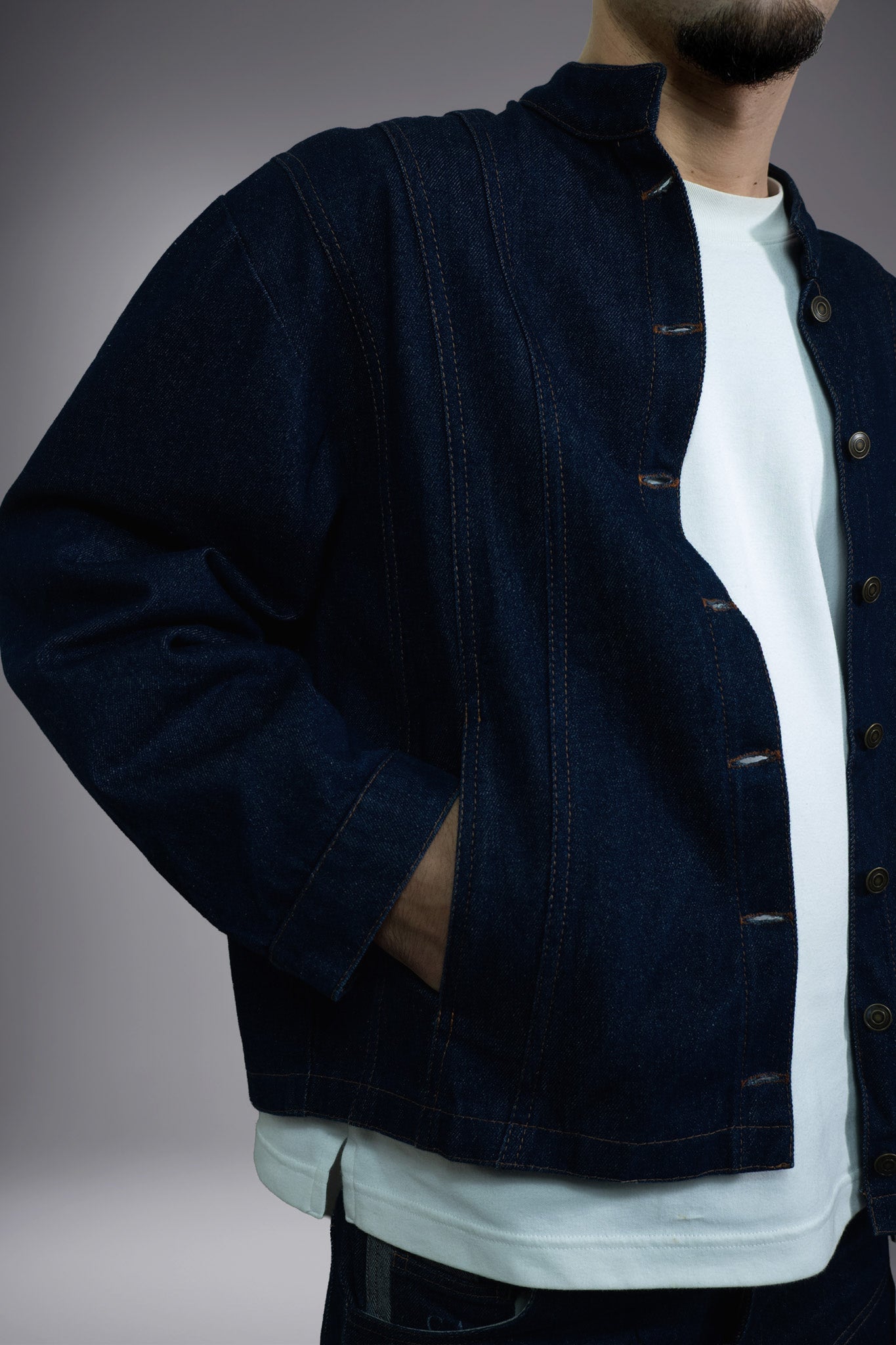 Close-up of a dark raw denim jacket with contrast stitching, button closure, side pocket and structured collar. - Motor Cycle Brut