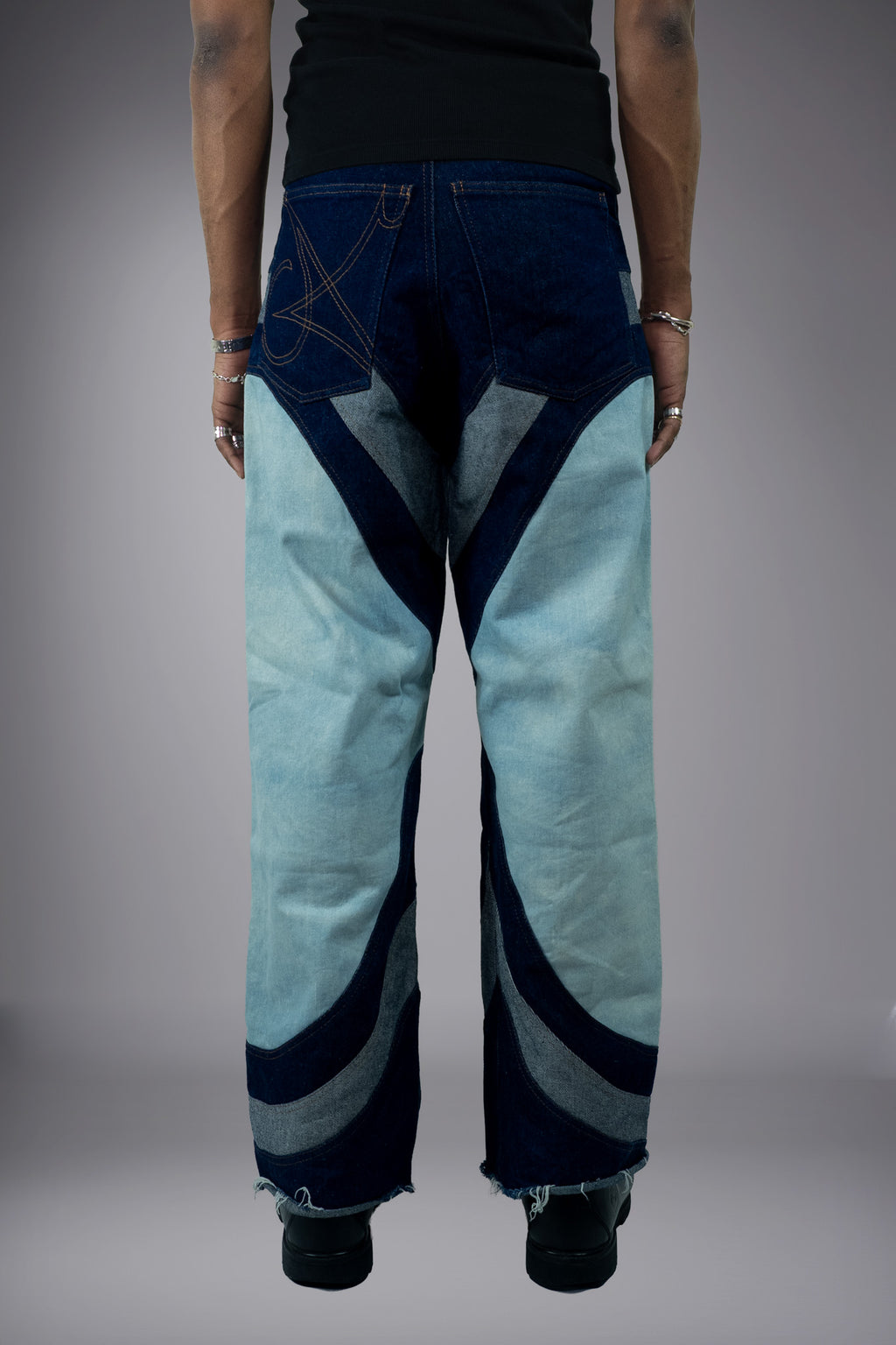 Back view of two-tone wide-leg denim jeans with light wash panels, dark curved inserts, graphic pocket stitching and raw hem details. - Motor Cycle Triple Jean