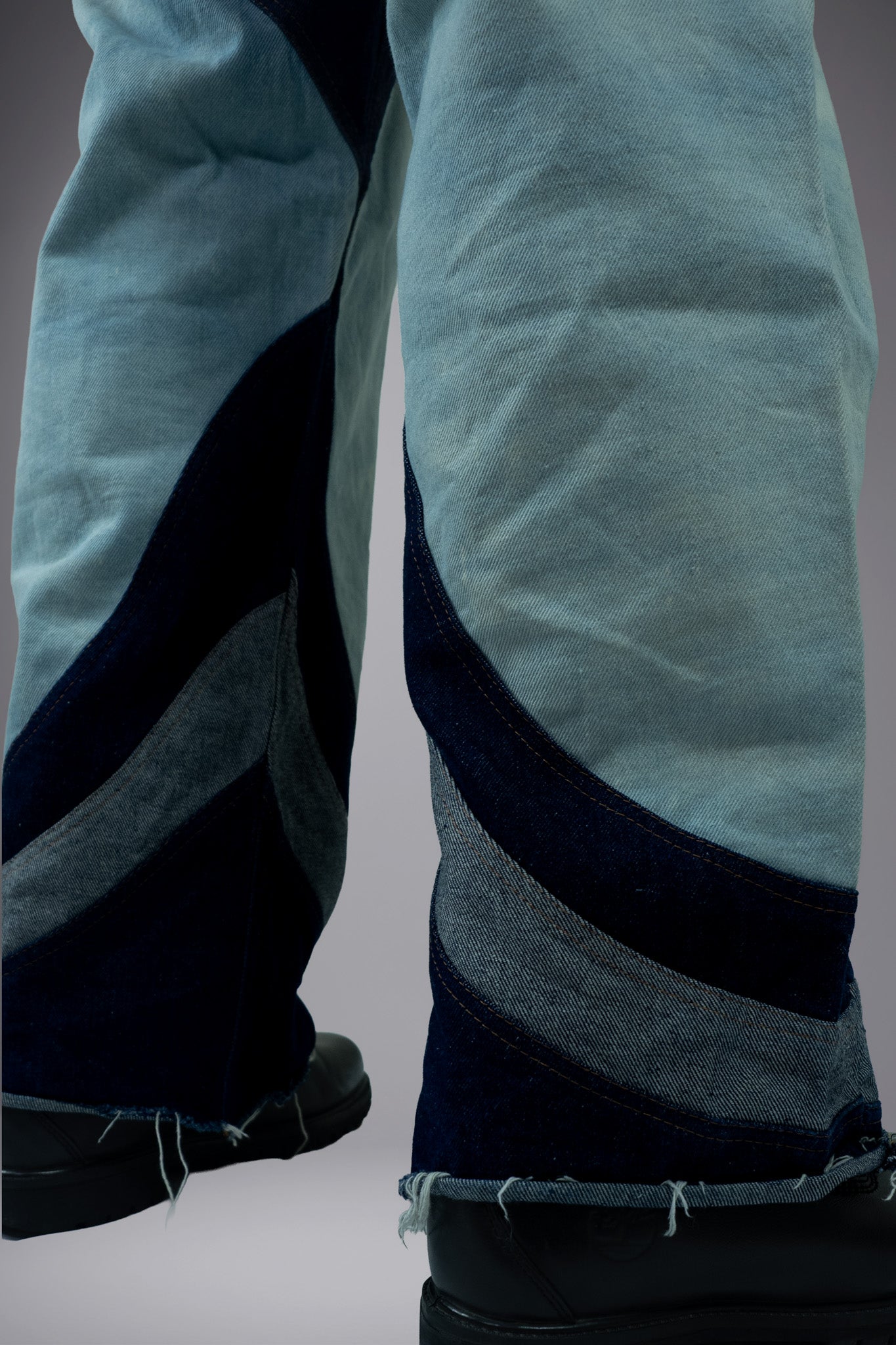 Close-up of two-tone denim jeans with curved dark panels, light wash fabric and raw hem construction. - Motor Cycle Triple Jean